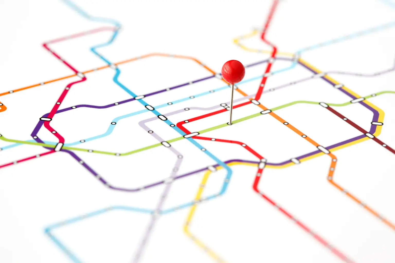 A computer-generated fictional map of train lines, containing colourful lines criss-crossing the page. A red pin clothespin sticks from up from the centre of the paper.